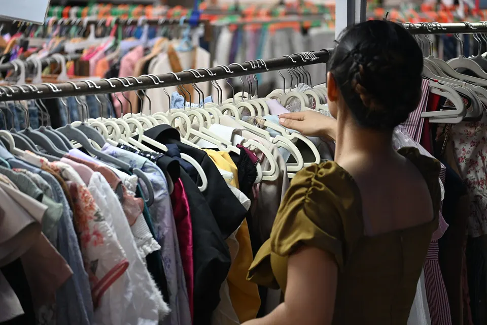 A shopper browsing a crowded rack of colourful dresses and tops in a secondhand clothing shop